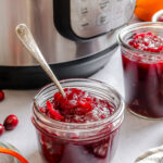 A small glass jar with cranberry sauce next to an Instant Pot.