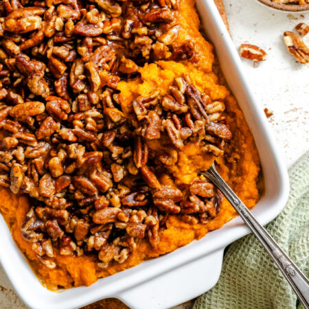 A silver spoon holding a scoop of sweet potato casserole in a dish.