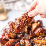 A hand holding a wing over a platter of sesame ginger wings.