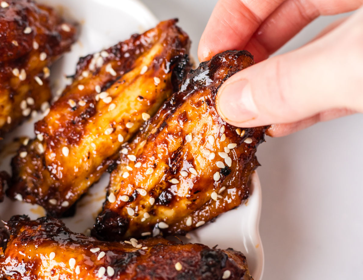 A hand with fingers grabbing a sesame ginger wing on a platter.